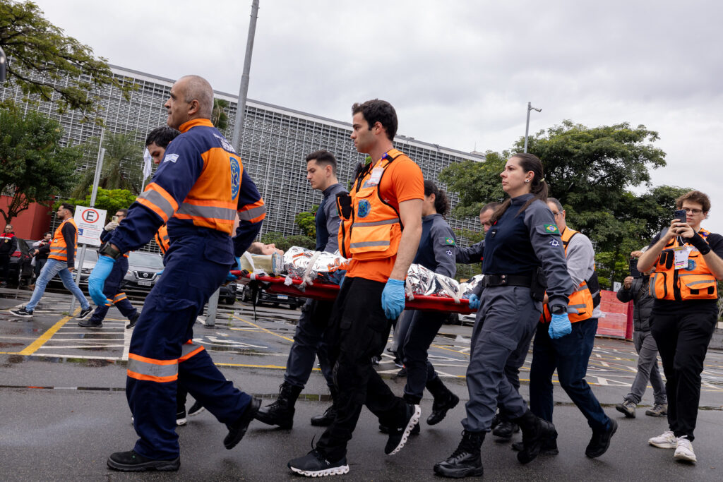 Agentes de Defesa Civil e de segurança pública conduzem maca durante simulado de resposta a desastre