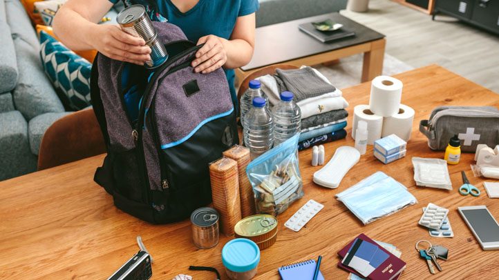 Itens organizados de uma mochila de emergência: garrafas de água, lanterna, kit de primeiros socorros e documentos protegidos em saco plástico.