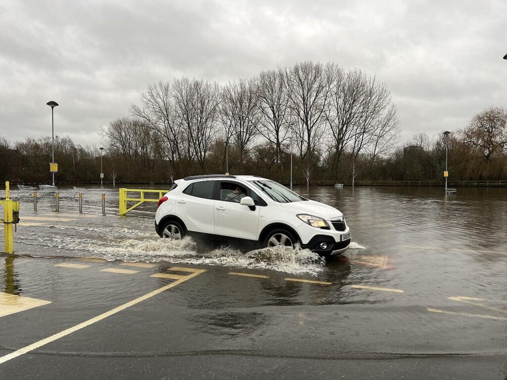 Rua alagada com um carro parcialmente submerso, ilustrando o tipo de cenário de alagamento urbano abordado no texto.